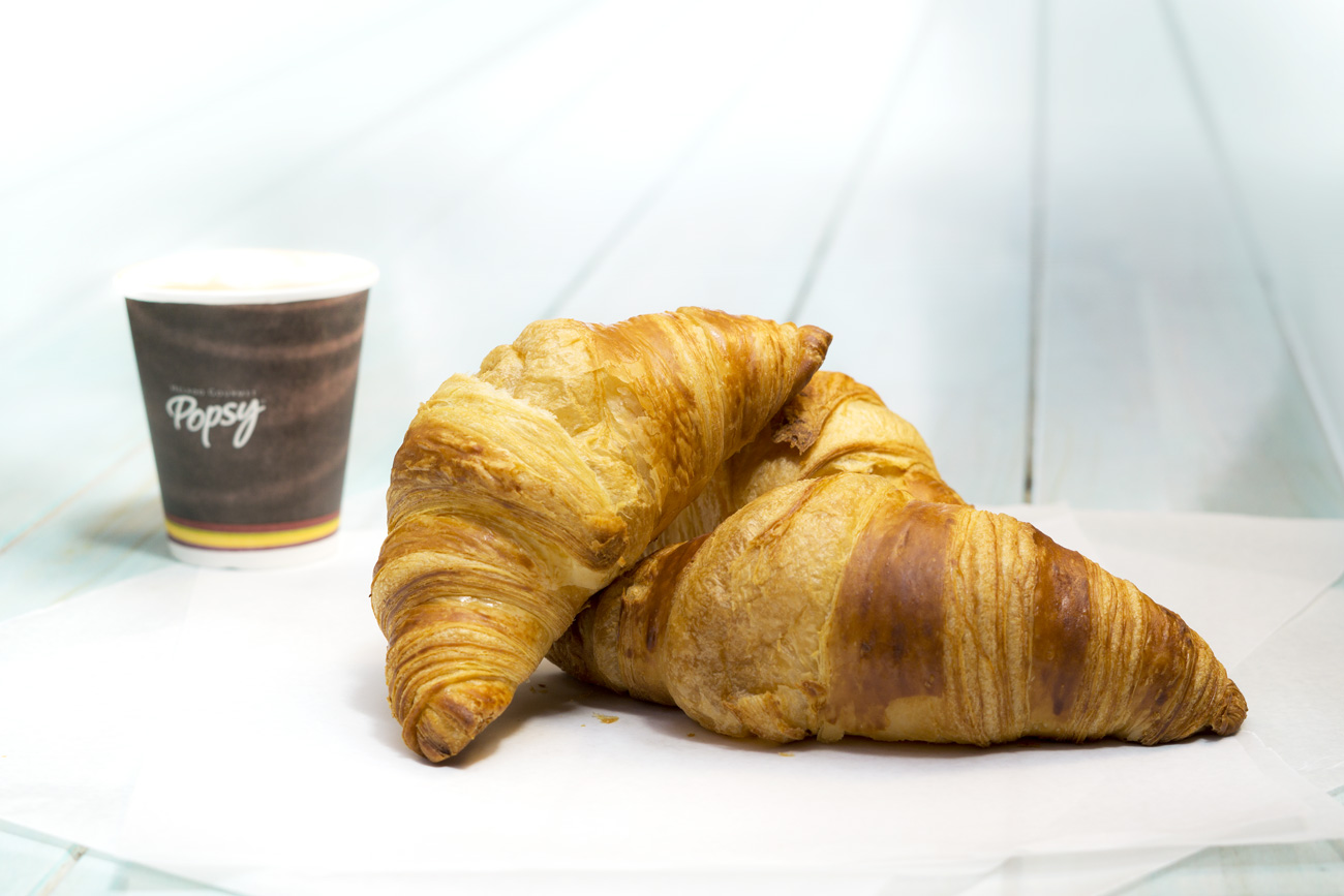 Fotografía de croissant y un vaso de café al fondo